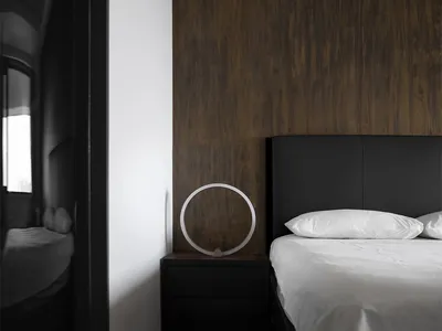 Modern minimalist bedroom featuring black leather headboard, wooden accent wall, and glass lamp on black nightstand.