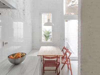 Modern minimalist kitchen with marble countertops and wooden dining table and chairs.