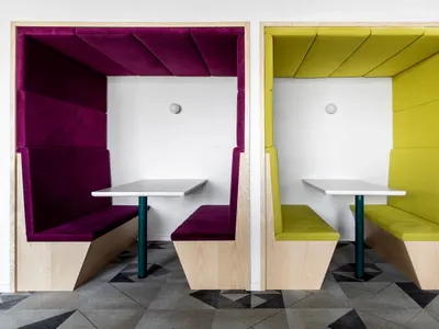 A photograph of two modern cafe booths with purple and yellow upholstered walls and white tables.