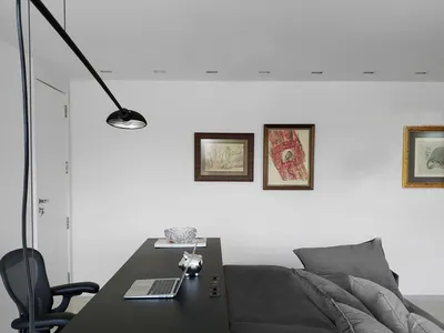 Minimalist bedroom featuring black furniture against a white wall with framed artwork.