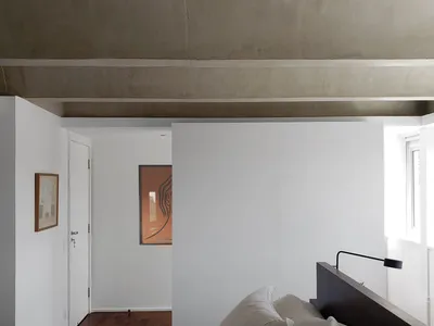 A minimalist bedroom featuring a concrete headboard, white bedding, and a simple, uncluttered space.