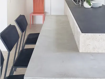 A modern, minimalist kitchen with a concrete countertop and black chairs.
