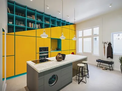 A minimalist kitchen featuring bright yellow lacquered cabinets, a green metal structural element, and a marble kitchen islan