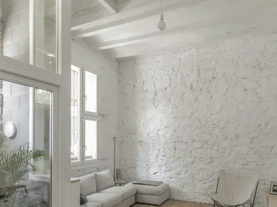 Minimalist living room with concrete walls and floor, featuring a white couch and a woven rug.