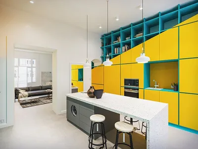 Modern kitchen with yellow and teal cabinets, white countertops, and pendant lights.