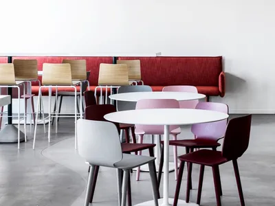 A modern restaurant interior with white tables, colorful chairs, and a red bench seating area.