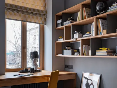 A modern home office with a wooden desk and shelves filled with books and toys.