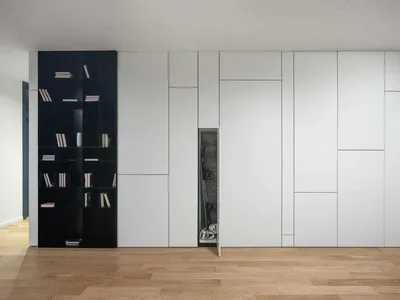 A minimalist bedroom with white paneling, black shelving, and a hidden storage compartment.
