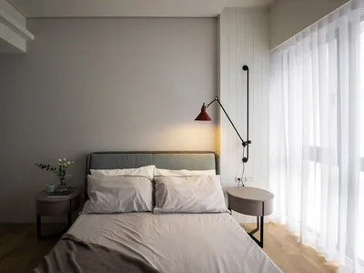 A minimalist bedroom with a bed, side tables, and a wall-mounted lamp.