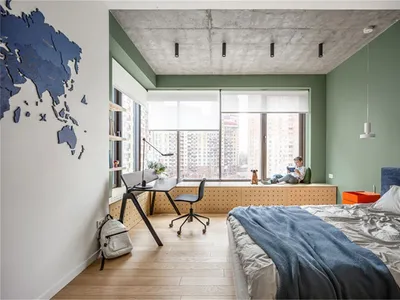A minimalist bedroom with a concrete ceiling, wooden floor, and a green wall. There is a bed with blue bedding, a desk area,