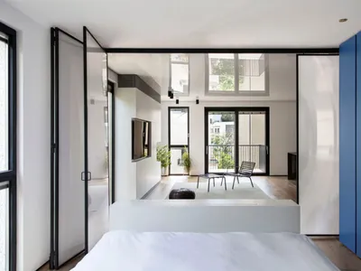 Modern minimalist bedroom with white walls, glass walls, and wood flooring.