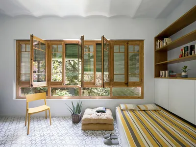 A minimalist bedroom with a large window, wooden furniture, and a striped rug.
