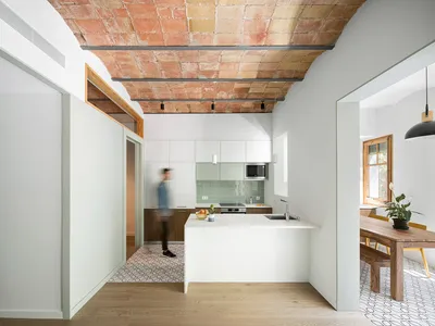 A minimalist kitchen with white cabinets, a central island, and a tile floor.