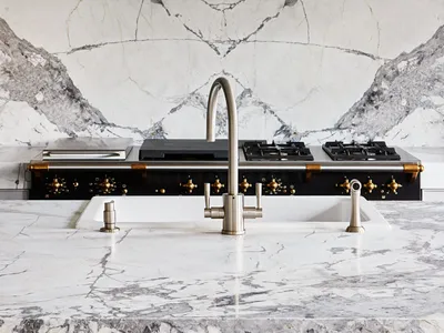 A modern kitchen featuring a marble countertop and backsplash, with a stainless steel faucet and stove.