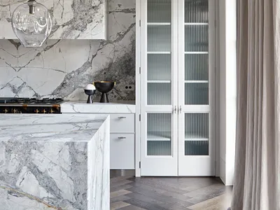 A modern kitchen with marble countertops and flooring, featuring white cabinetry and a minimalist design.