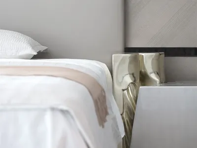 Modern, minimalist bedroom featuring a bed with metallic headboard and metallic side tables.