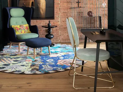 A modern industrial living room featuring brick walls, a round floral rug, and a combination of green and blue upholstered ch