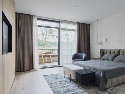 A modern minimalist bedroom with grey bedding, a upholstered bed frame, and a flat-screen TV mounted on the wall.