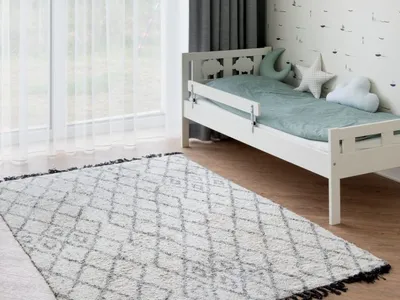 A minimalist bedroom with a wood frame bed, grey curtains, and a patterned rug.