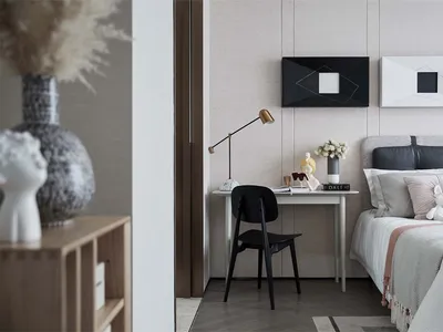 A cozy minimalist bedroom with a comfortable bed, decorative pillows, and a small desk with a lamp and vase.