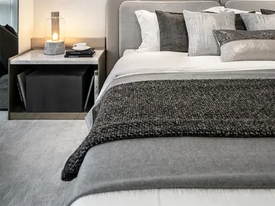 A modern bedroom with grey fabrics, including a bed with a grey headboard and multiple pillows, a marble nightstand with a la