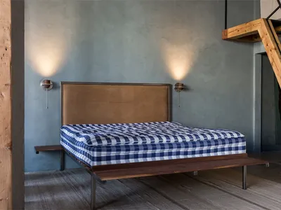A minimalist bedroom with a wooden bed frame, checkered bedspread, and a leather headboard.
