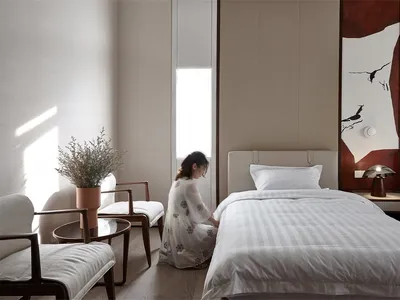 簡約臥室內擺放白色布藝床、植物與燈具。