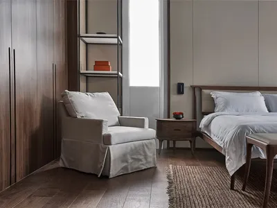 Modern minimalist bedroom featuring wood furniture, white bedding, and a soft armchair in a serene environment.