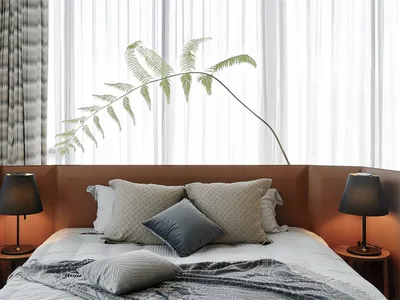 A minimalist bedroom with a bed adorned with multiple pillows, a blanket, and side tables with lamps and a plant.