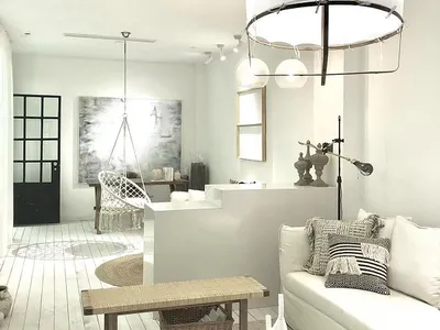 Minimalist living room with white and neutral color palette, featuring white couch, hanging chair, and modern lighting fixtur