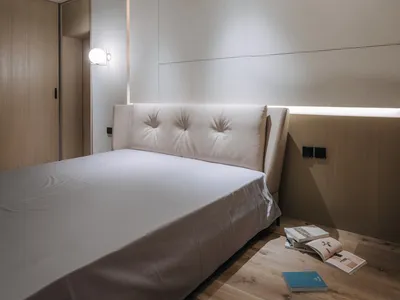 Bedroom with minimalist design, white bed, and wooden floor and headboard.