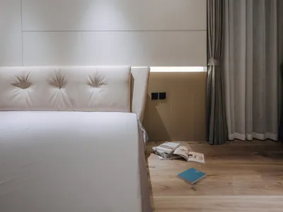 A minimalist bedroom with white wooden flooring, white headboard, and a few scattered books.