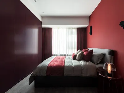A modern bedroom with a red accent wall, bed with mixed textiles, and a sleek, minimalist design.