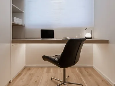 A minimalist office space featuring a desk with a laptop, a black chair, and a bookshelf.