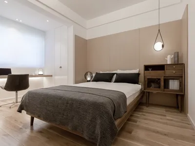 A minimalist bedroom with light wood flooring, a white bed, and black bedding.