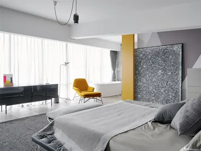 A modern minimalist bedroom featuring a bed with a gray blanket, leather headboard, and a yellow chair.
