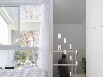 Minimalist bedroom with white walls, wooden floor, and large windows with sheer curtains.