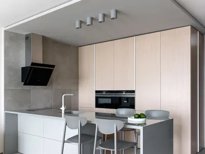 Minimalist residential kitchen with concrete countertops, light wood cabinets, and metallic stools on a wooden floor.