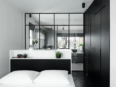 A minimalist bedroom features a sleek, black-and-white color palette, with a glass partition, wooden flooring, and metal fixt