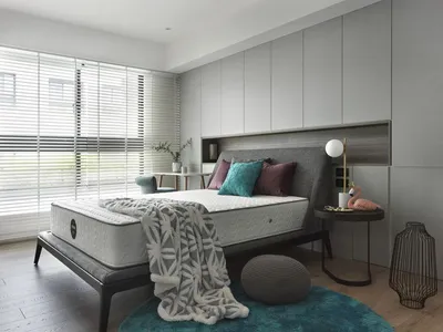 Modern minimalist bedroom with a grey upholstered headboard, turquoise and purple pillows, and a grey and white patterned bla