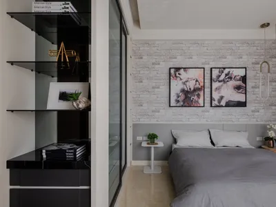 A minimalist bedroom with a brick accent wall, featuring a bed with gray bedding and a small table with a green plant.