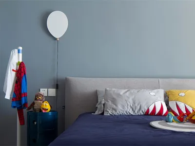 A modern bedroom with a gray upholstered headboard, blue bedding, and colorful plush toys.