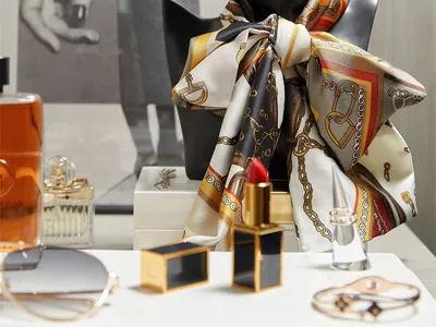 A black mannequin head adorned with a patterned scarf and gold dangling earrings, surrounded by various accessories such as p