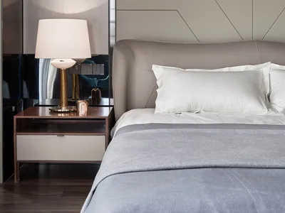 A minimalist bedroom with neutral-toned materials, showcasing a bed with white pillows and a gray blanket, accompanied by a m