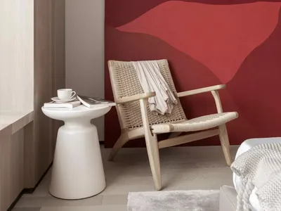 A minimalist bedroom with a wooden frame chair and a red abstract painting on the wall.