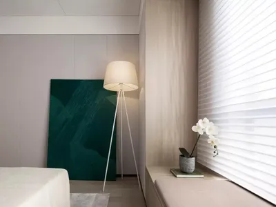 Modern minimalist bedroom with a white bed, green abstract artwork, white floor lamp, and light wood bench and walls.