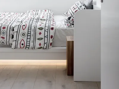 Minimalist bedroom with white walls, wooden floor, and patterned bedding.