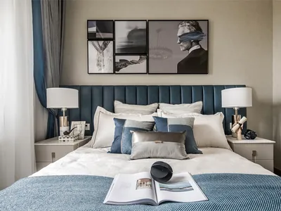 A modern bedroom featuring a bed with a blue upholstered headboard, white and gray bedding, and a variety of decorative pillo