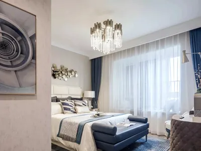 Modern bedroom featuring a bed with fabric headboard, blue leather bench, and glass chandelier.