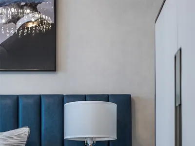 Modern bedroom with a blue upholstered bed, white nightstand, and marble lamp base.